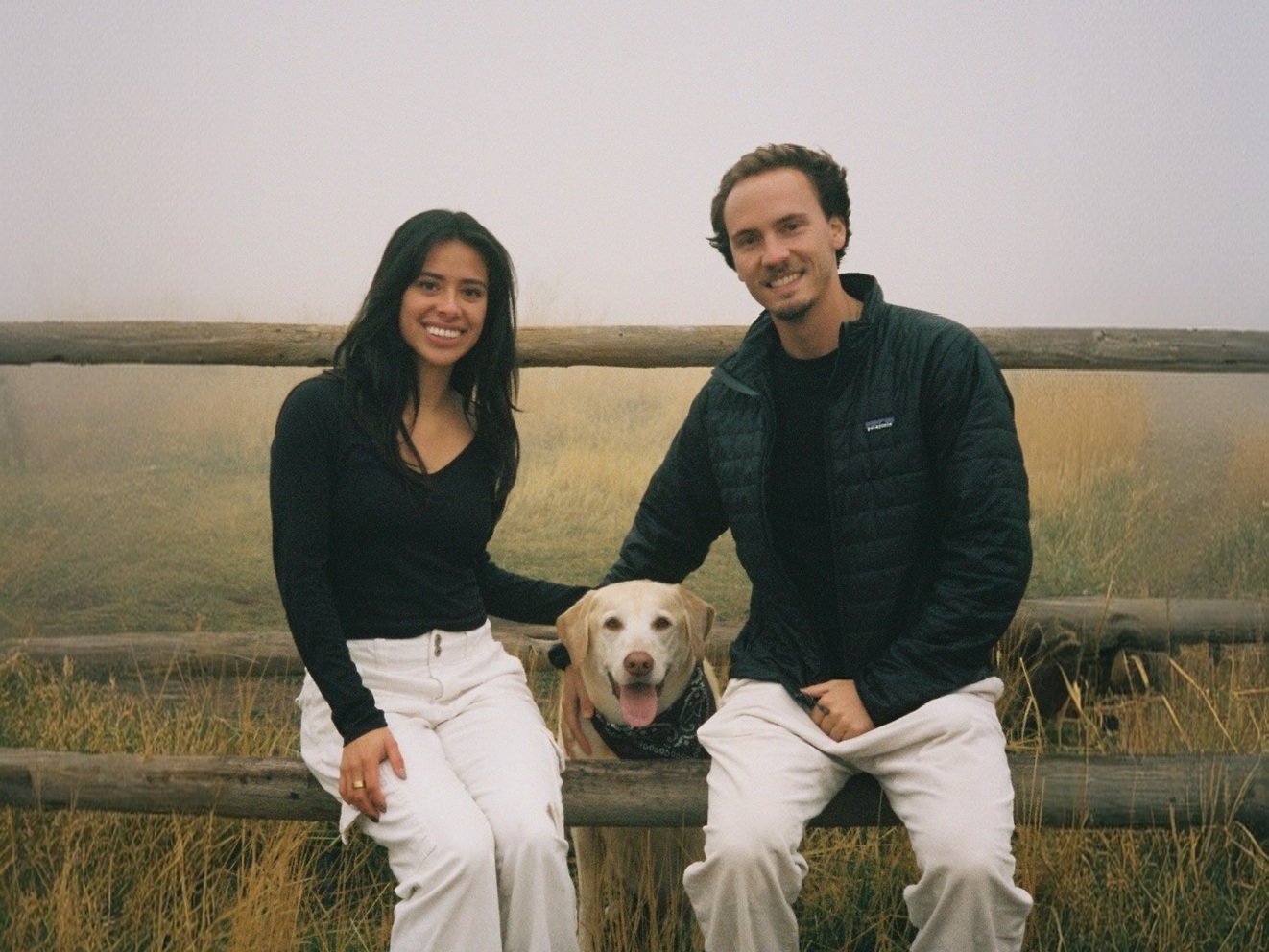 A couple and their dog sitting on a fence